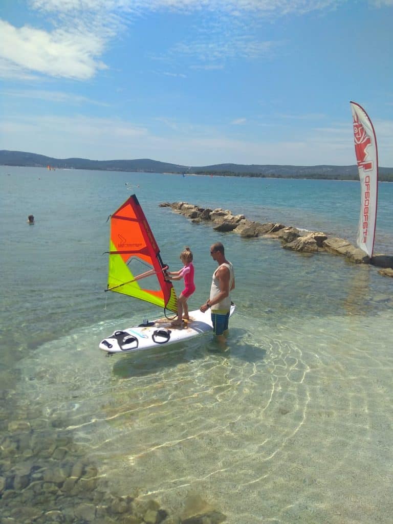 Kid on surf board with instructor learning to windsurf