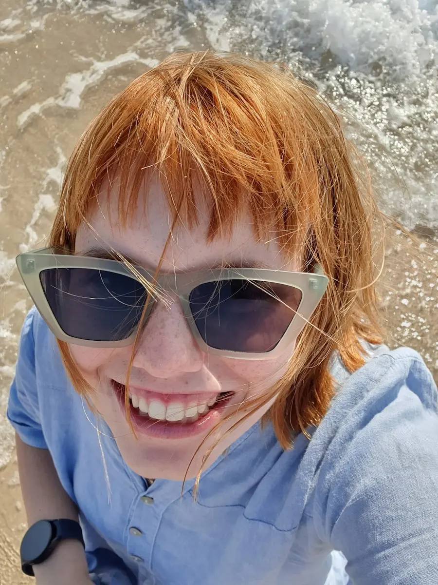 Nasmijana osoba s naočalama na plaži uz more