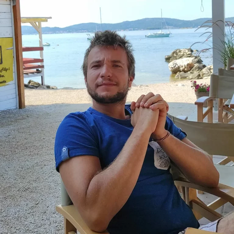 Muškarac sjedi u kafiću uz more i brodove