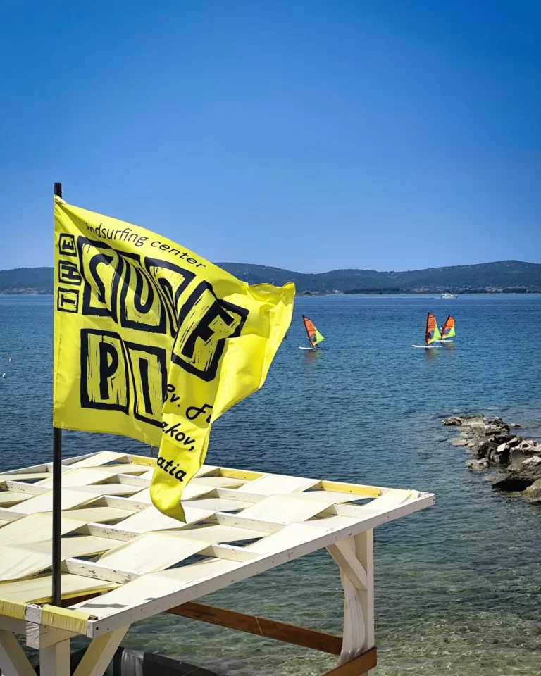 Žuta zastava surf centra uz more i jedriličari