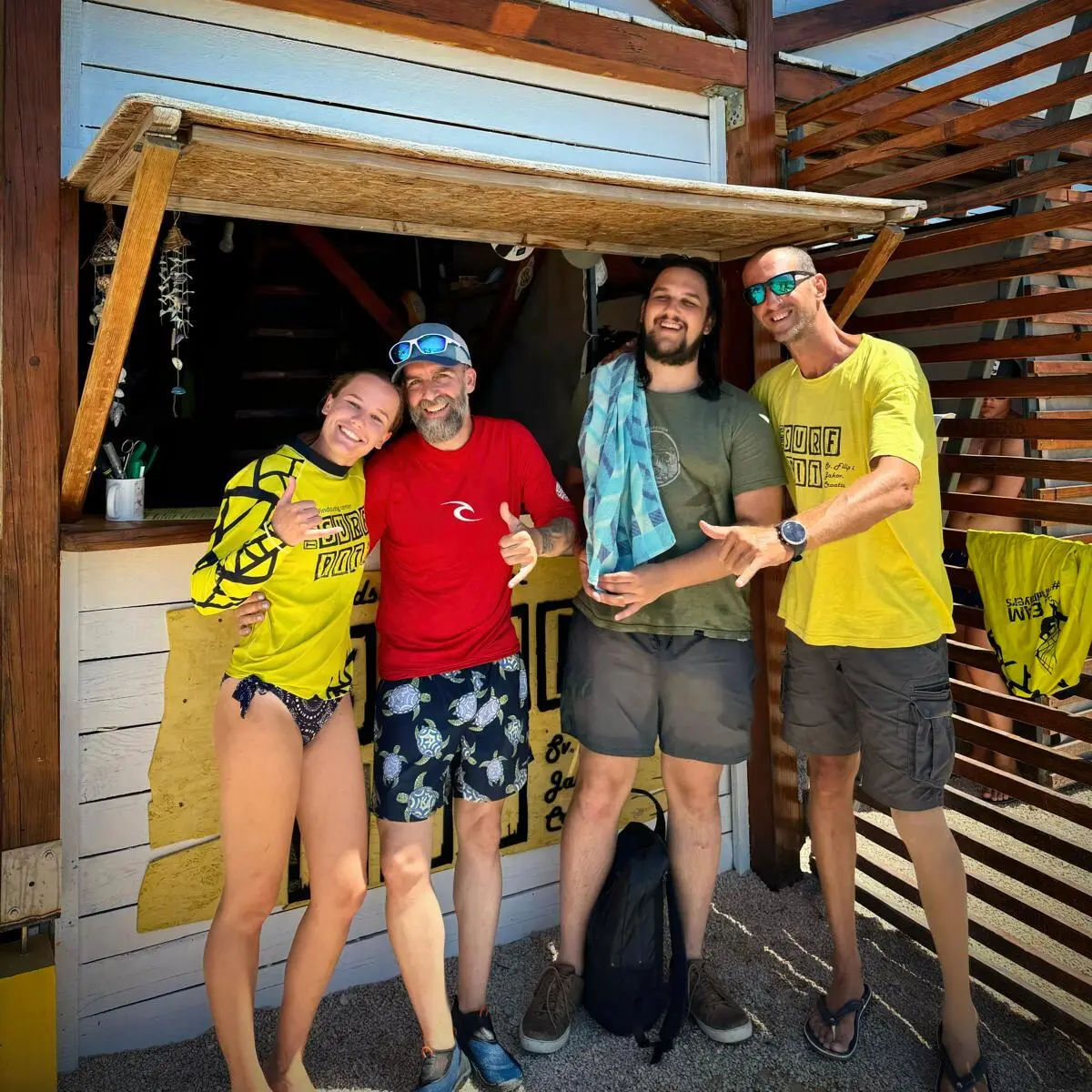 Četvero ljudi pozira ispred drvene kućice na plaži
